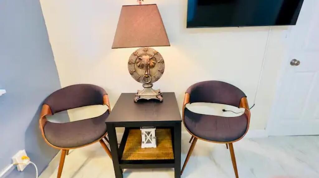 A small table with two chairs, a decorative lamp, and a television mounted on the wall.