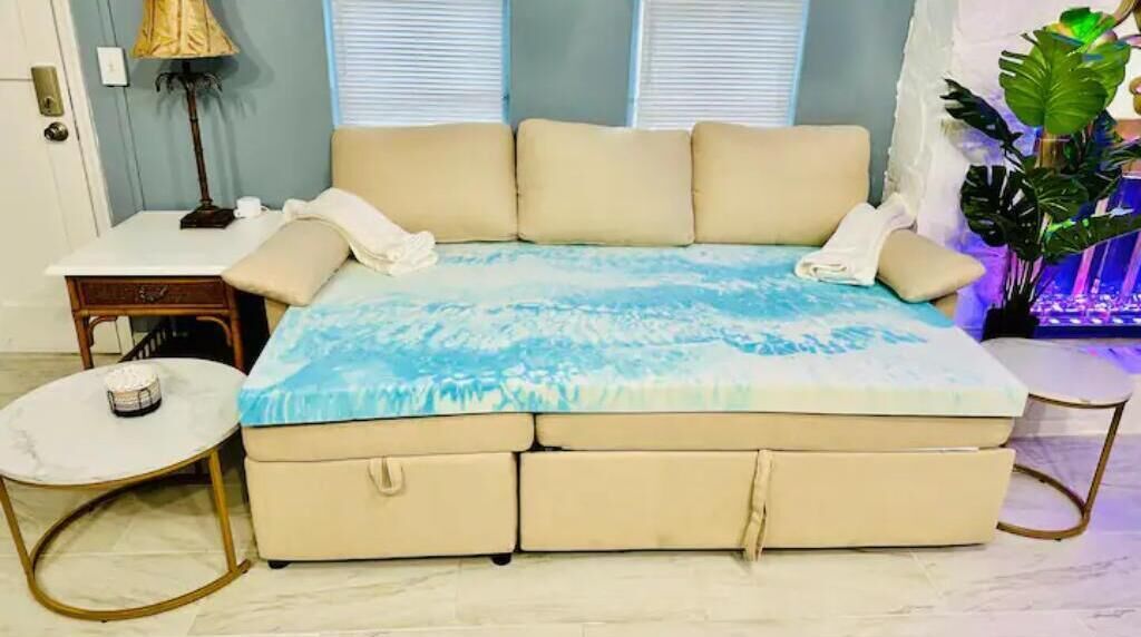 Un lit recouvert d’une couvre-lit à motifs bleus et blancs, une table de chevet avec une lampe, et une petite table ronde également dotée d’une lampe.