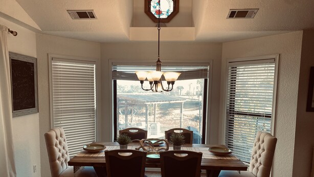 A dining area with a table set for four, surrounded by chairs, with a view of a landscape through large windows. - Beautiful home on Lake Hamilton  ! (Lake Hamilton)