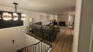 Ein geräumiges Wohnzimmer mit Kamin aus Stein, einer Ledersofa und einer Treppe mit schwarzer Geländer.