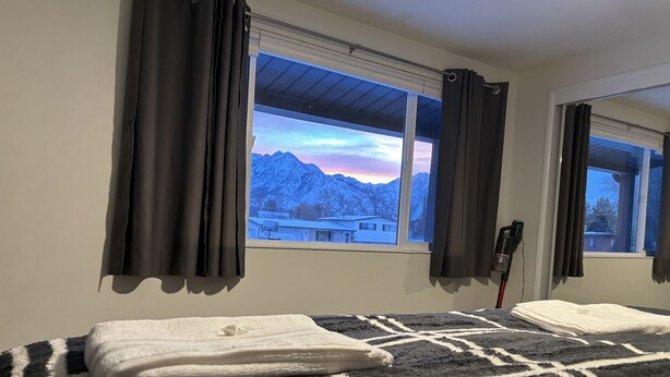Ein Hotelzimmer mit Bett, einem Fenster mit Vorhängen und Blick auf Berge.