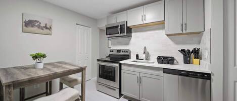 Una cocina moderna con armarios blancos, electrodomésticos de acero inoxidable y una mesa de comedor de madera con bancos.