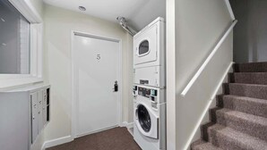 A laundry room with a washing machine and dryer, a door with a number, and a carpeted floor. - Modern 2BD Apartment Near Royal Oak (Hazel Park)