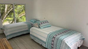 Een kamer met twee bedden, een houten tafel en een groot raam met uitzicht op groen.