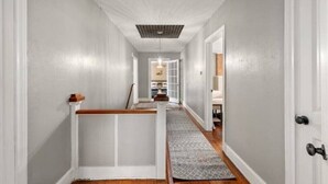 A hallway with a wooden railing, a patterned rug, and a door on the right.