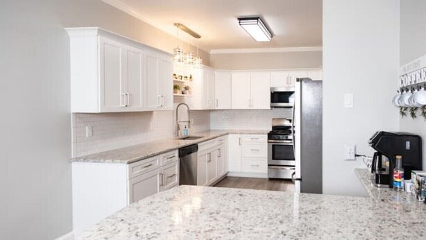 A modern kitchen with white cabinets, a granite countertop, stainless steel appliances, and a coffee machine.