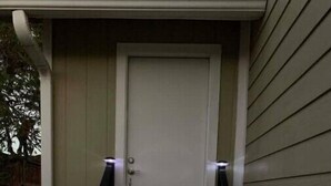 A wooden staircase leading to a white door with a black railing and small lights at the top of the steps.