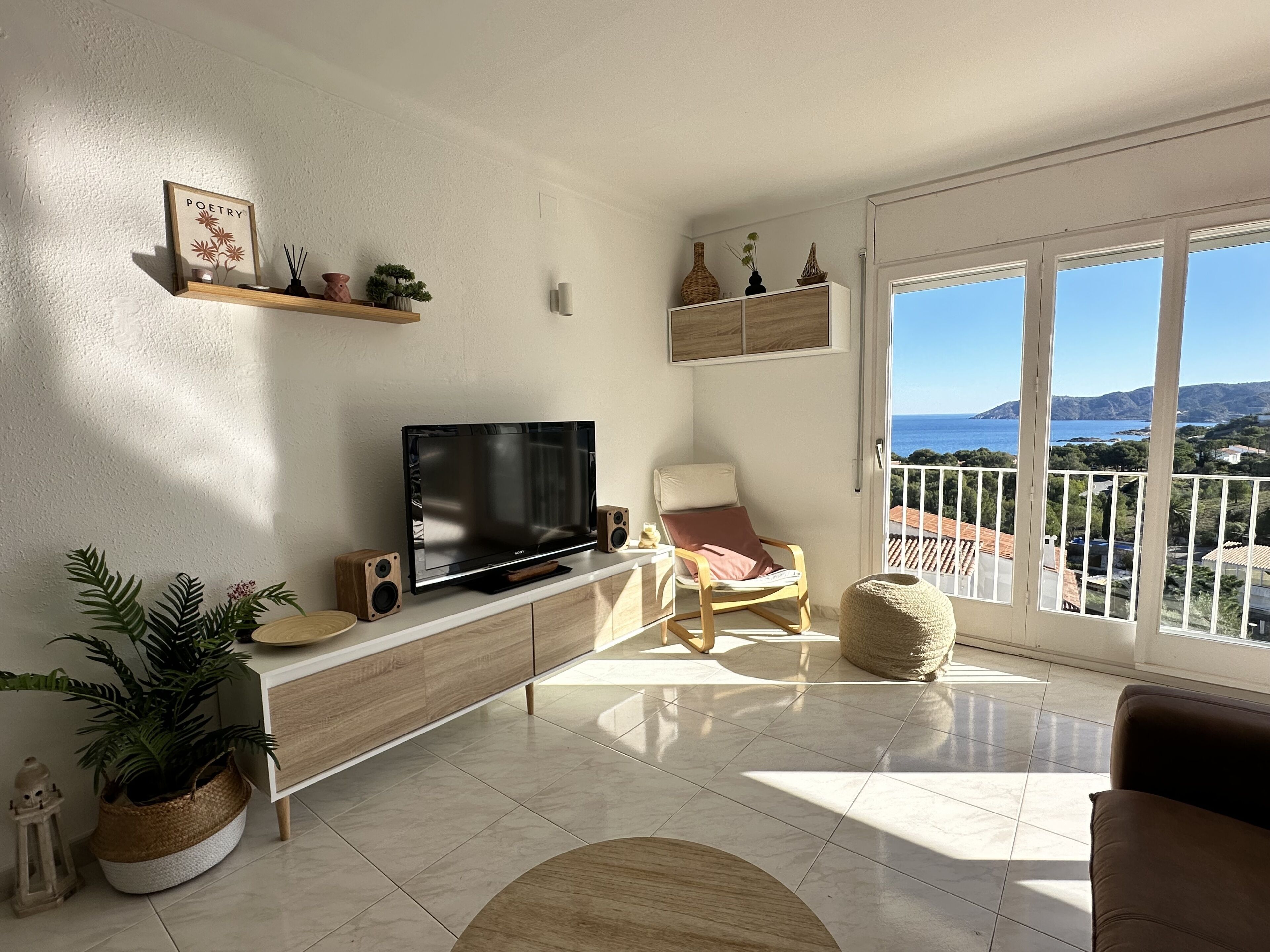 Una sala de estar moderna con televisión de pantalla plana, muebles de madera, una planta en maceta y vista al mar.
