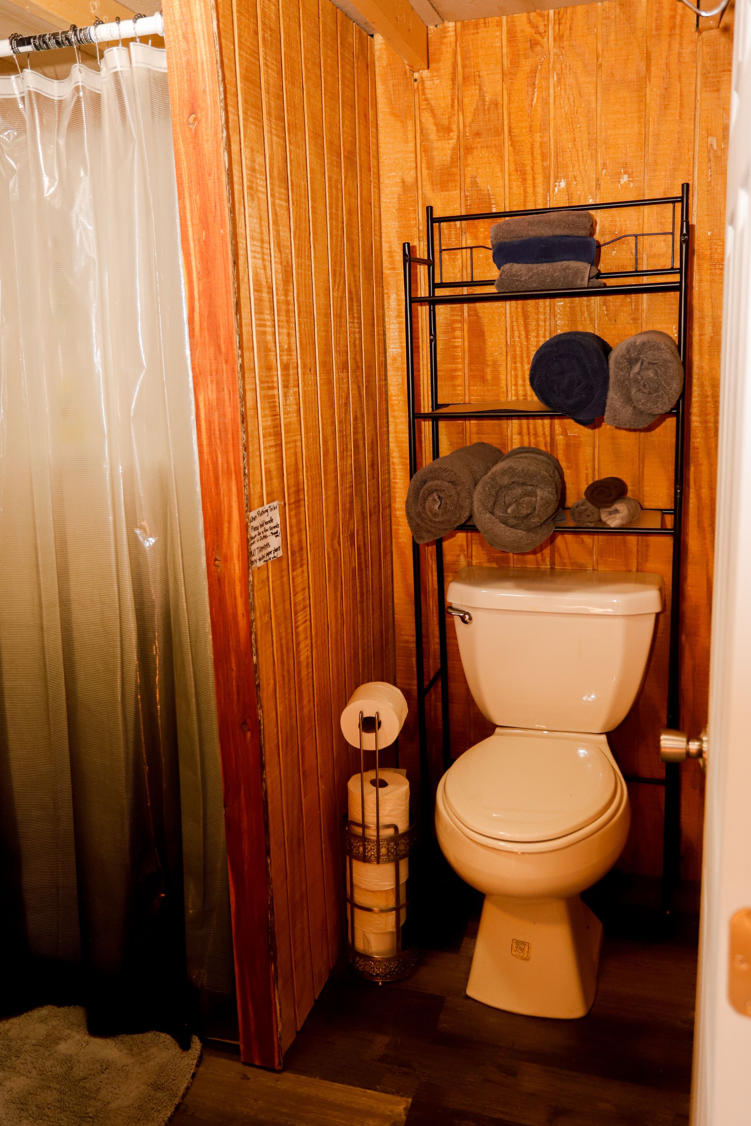 Un baño con paneles de madera, un inodoro, un perchero con toallas, una cortina de ducha y un dispensador de papel higiénico.