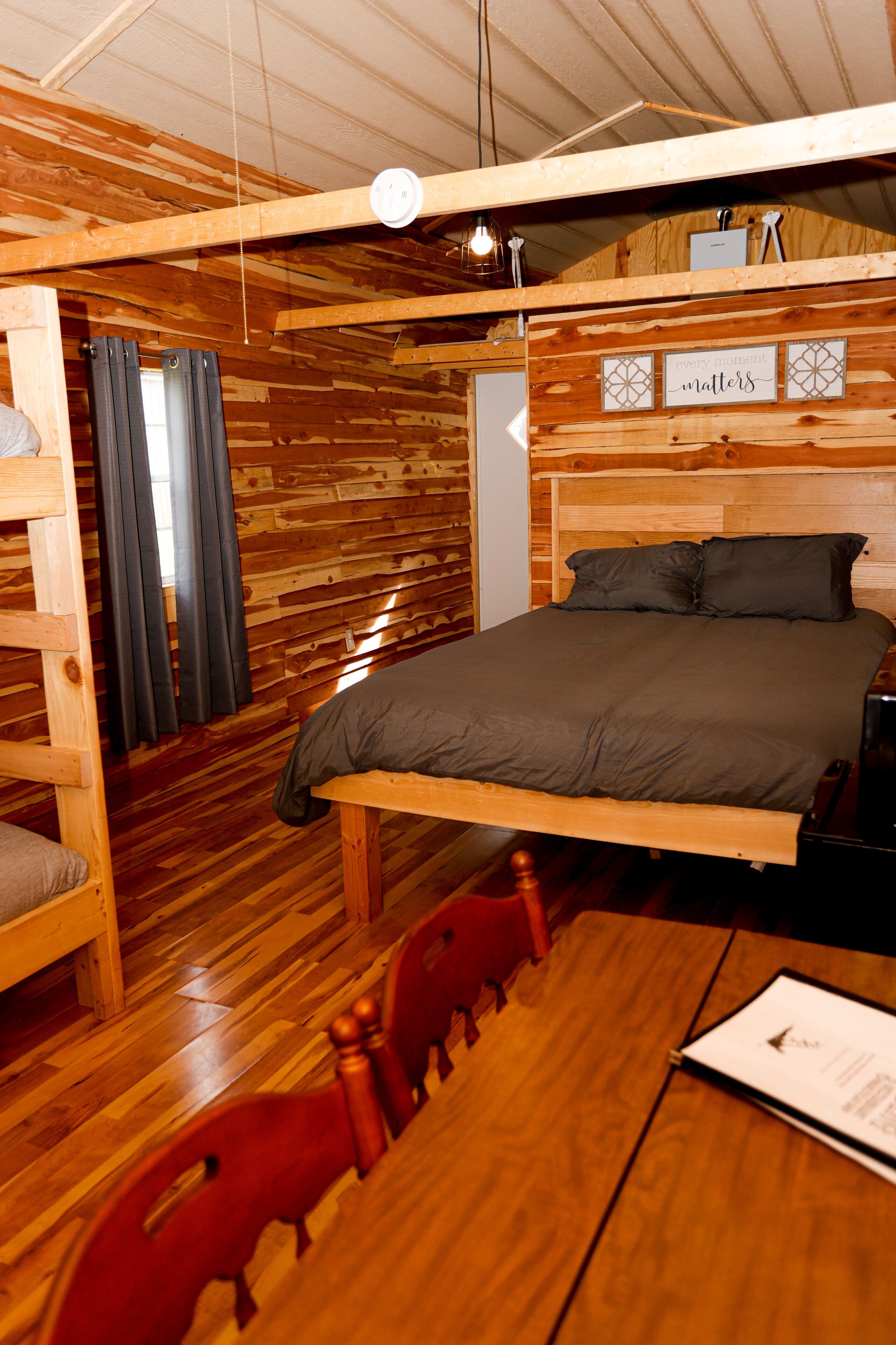 Una habitación tipo cabaña de madera con cama, una mesa y una silla.