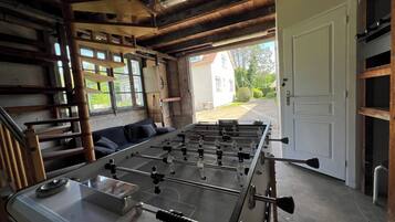 Une pièce avec un baby-foot, un canapé et une vue sur une maison, visible à travers une porte ouverte.