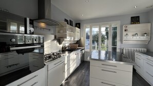 A modern kitchen with white cabinetry, a gas stove, and a built-in oven. There is a window providing natural light and a view of the outdoors. - Les Sablons - Villa 15pers - table football darts bbq (La Houssaye-en-Brie)