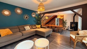 A modern living room with a sectional sofa, two small tables, and a dining area with a long table and chairs. - Les Sablons - Villa 15pers - table football darts bbq (La Houssaye-en-Brie)