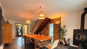 A spacious dining area with a wooden table and chairs, a staircase, and a modern fireplace. - Les Sablons - Villa 15pers - table football darts bbq (La Houssaye-en-Brie)