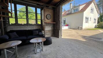 A rustic interior with a wooden ceiling, a black sofa, two metal tables, and a dartboard.