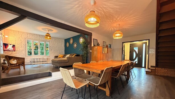 A spacious living area with a large wooden dining table, wicker chairs, and a sofa with cushions. There are two pendant lights hanging from the ceiling. - Les Sablons - Villa 15pers - table football darts bbq (La Houssaye-en-Brie)