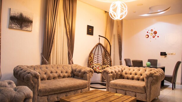 A living room with two tufted sofas, a wooden coffee table, a hanging chair, and a dining area with chairs and a table. - 4 Bedroom Fully Detached Duplex in Lekki, Lagos (Lekki)