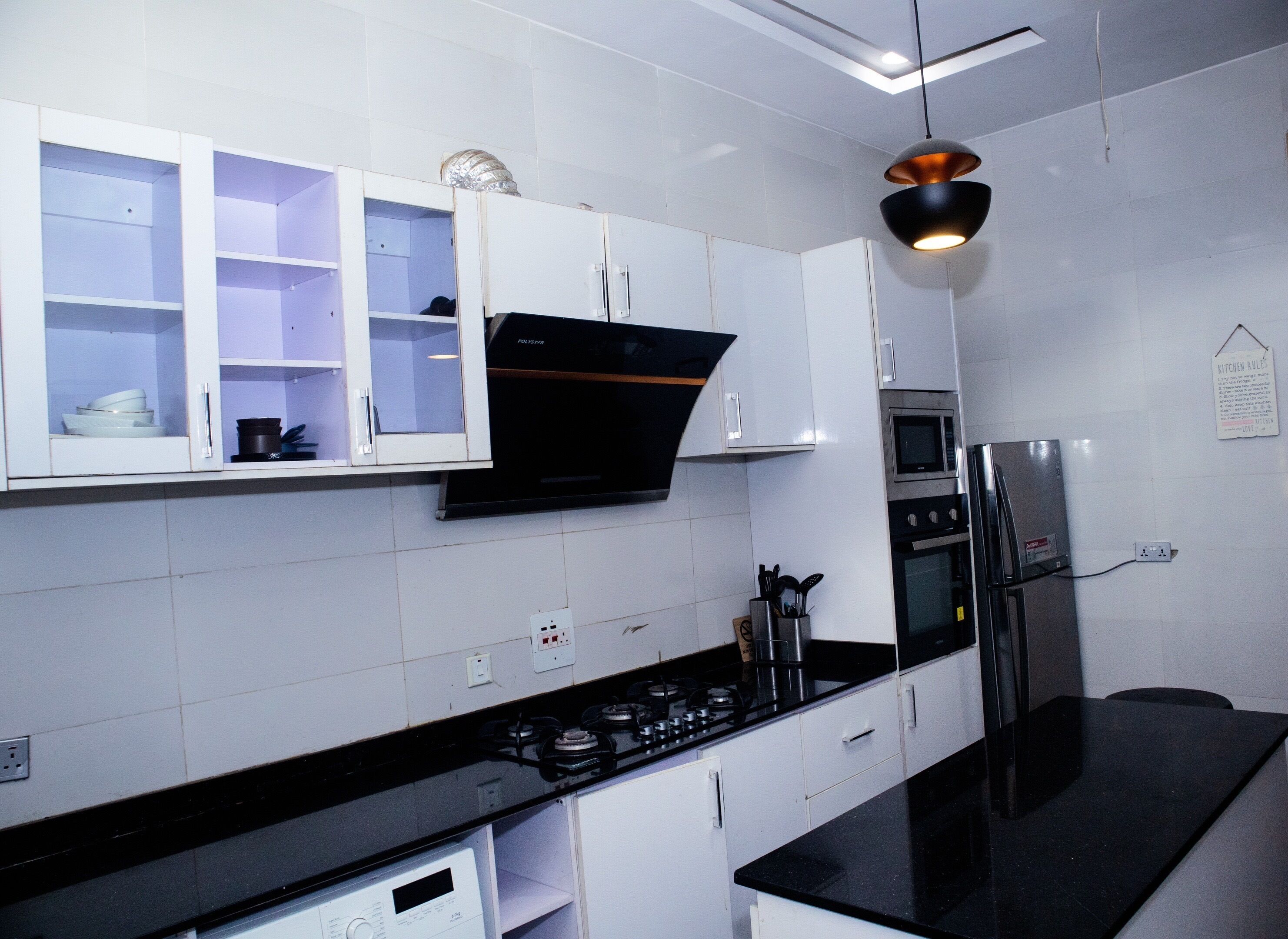 A modern kitchen with white cabinets, a black countertop, a gas stove, an oven, a microwave, and a hanging pendant light.