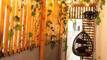 Un pasillo estrecho con listones de madera y plantas colgantes, un sillón colgante y un pequeño rincón de estar con cojines.