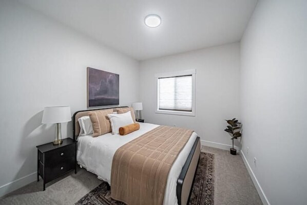 A bedroom with a bed, bedside tables, a window, and a painting on the wall.