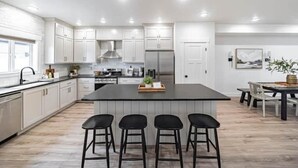 Eine moderne Küche mit weißen Schränken, einer zentralen Kochinsel mit Barhocker und einem Essbereich mit Tisch und Stühlen.
