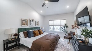 Ein Schlafzimmer mit Bett, Nachttisch, Kommode, Deckenventilator und Fernseher an der Wand.