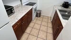 A compact kitchen with wooden cabinets, a microwave, a stove, and a sink.
