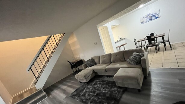 A living room with a sofa, a rug, a staircase, and a dining area.