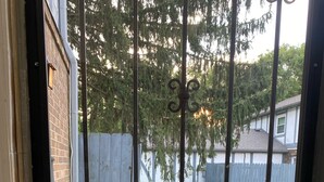 A metal gate with decorative elements, a brick wall, and a view of a grassy yard with a wooden fence and trees.
