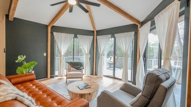 A cozy living room with a leather sofa, a round coffee table, and a gray armchair. There is a large window with white curtains, and a ceiling fan is visible. - Experience nature's charm! Retreat near Bryce Resort/George Washington Forest (Basye)
