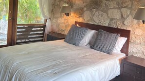 A bedroom with a wooden ceiling, a bed with white bedding, patterned pillows, a nightstand, and a stone wall. - Hibiscus House Oceanfront Paradise in Fernandez Bay (New Bight)