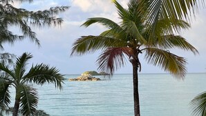 A beach with palm trees, a small island in the distance, and a boat on the sand. - Hibiscus House Oceanfront Paradise in Fernandez Bay (New Bight)