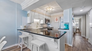 Une cuisine moderne avec des meubles blancs, un comptoir noir et un tabouret de bar.