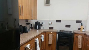 A compact kitchen with wooden cabinets, a black refrigerator, a stove, and a coffee maker.