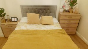 A neatly made bed with a grey tufted headboard, two beige pillows, and a mustard-colored blanket.