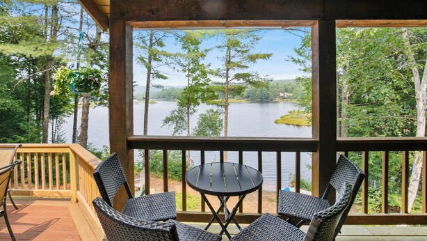A wooden deck with a table and chairs overlooking a lake surrounded by trees.