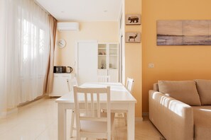 A dining area with a white table and chairs, a white cabinet, and a beige sofa.