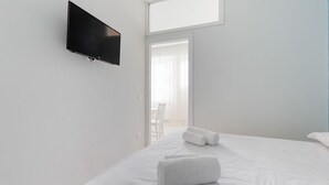 Habitación de hotel con cama, televisor de pantalla plana montado en la pared y vista al exterior por una ventana.