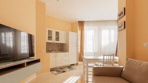 Una sala de estar moderna con un televisor de pantalla plana, un sofá, un comedor con mesa y sillas, y una cocina con armarios y salpicadero de azulejos.