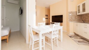 Un espacio habitable compacto con comedor, kitchenette y televisor montado en la pared.
