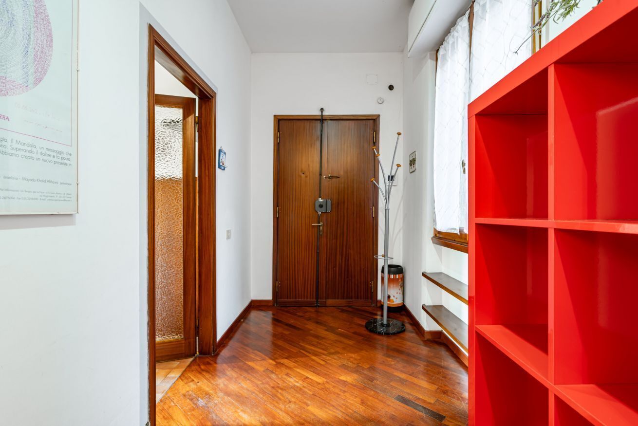 Un couloir doté d’un plancher en bois, d’une étagère rouge et d’une porte avec une serrure.