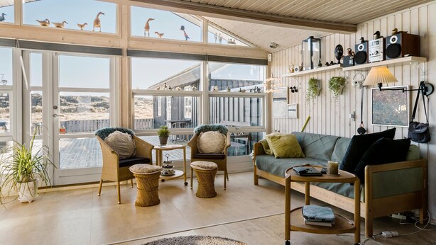 Un salon spacieux doté de grandes fenêtres, de meubles en osier, d’un canapé vert et d’une table basse en bois.