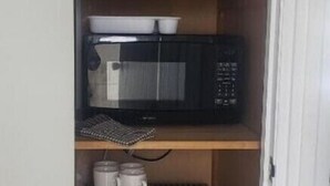 A compact kitchen with a microwave, a mini-fridge, and a coffee maker on the shelves.