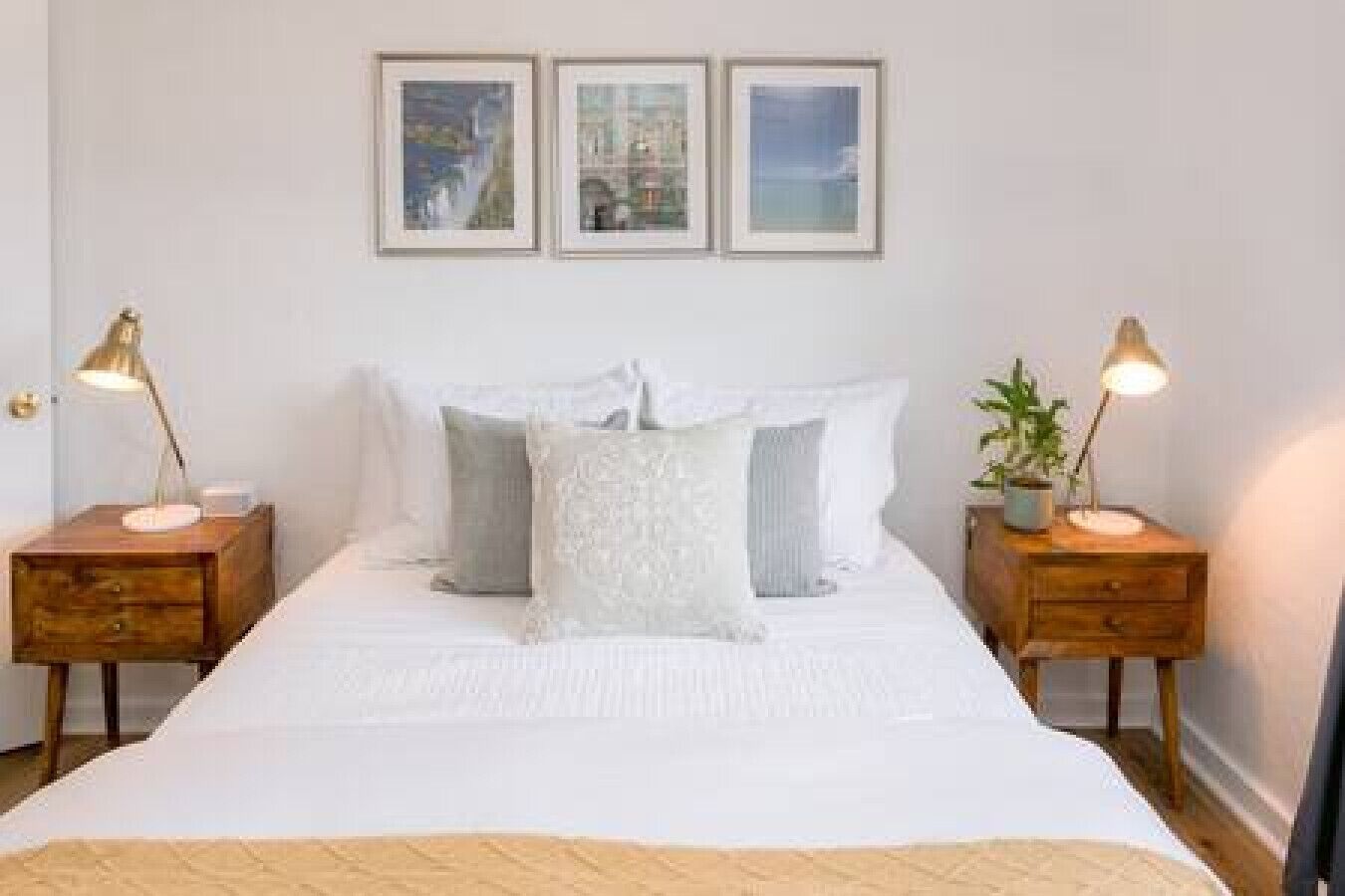 A neatly arranged bedroom with a large bed, two bedside tables with lamps, and three framed pictures on the wall.