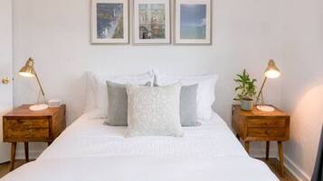A neatly arranged bedroom with a large bed, two bedside tables with lamps, and three framed pictures on the wall.