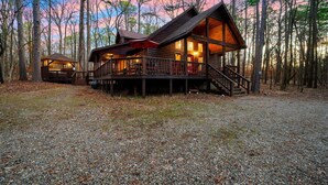 A cabin with a deck and a covered porch, surrounded by trees. - Oar & Arrow · Wilderness Retreat: Hot Tub, Grill, King Suites (Broken Bow)