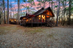 A cabin with a deck and a covered porch, surrounded by trees. - Oar & Arrow · Wilderness Retreat: Hot Tub, Grill, King Suites (Broken Bow)