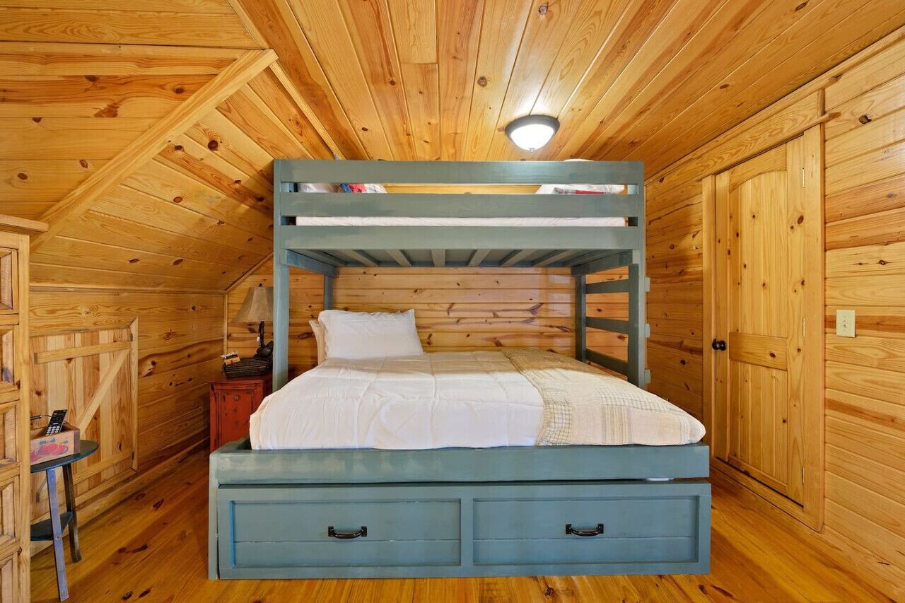 A bunk bed with a desk and chair, wooden walls, and a sloped ceiling.