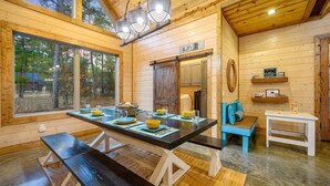 A wooden cabin interior with a dining table set for four, a bench, a small white table, and a blue bench with cushions. - The Copper Hideout · Hochatown Hideout: Hot Tub, Fire Pit, Pure Relaxation (Broken Bow)