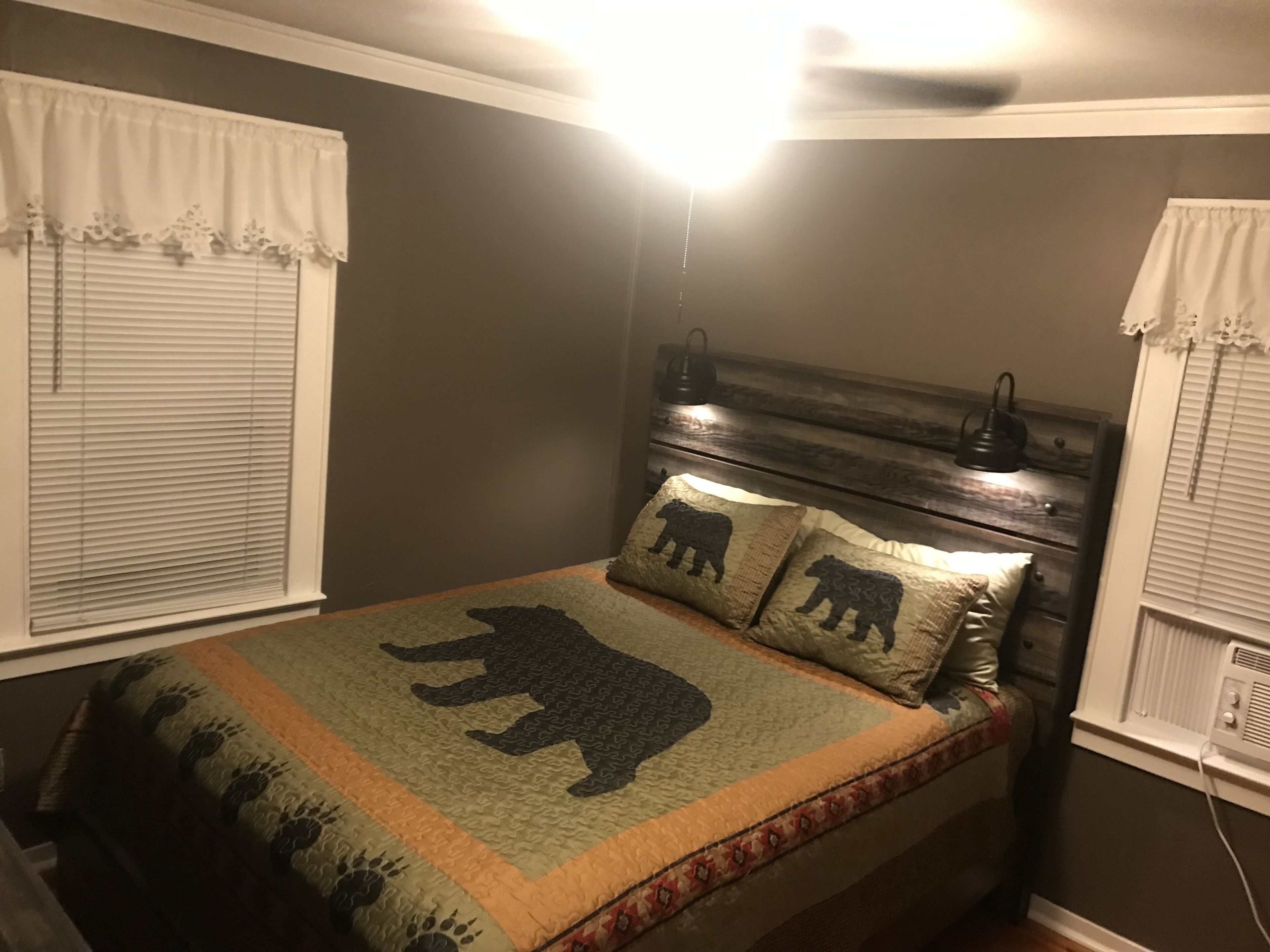 Un dormitorio con cama, colcha con diseños de osos, cabecera de madera y una lámpara de noche.